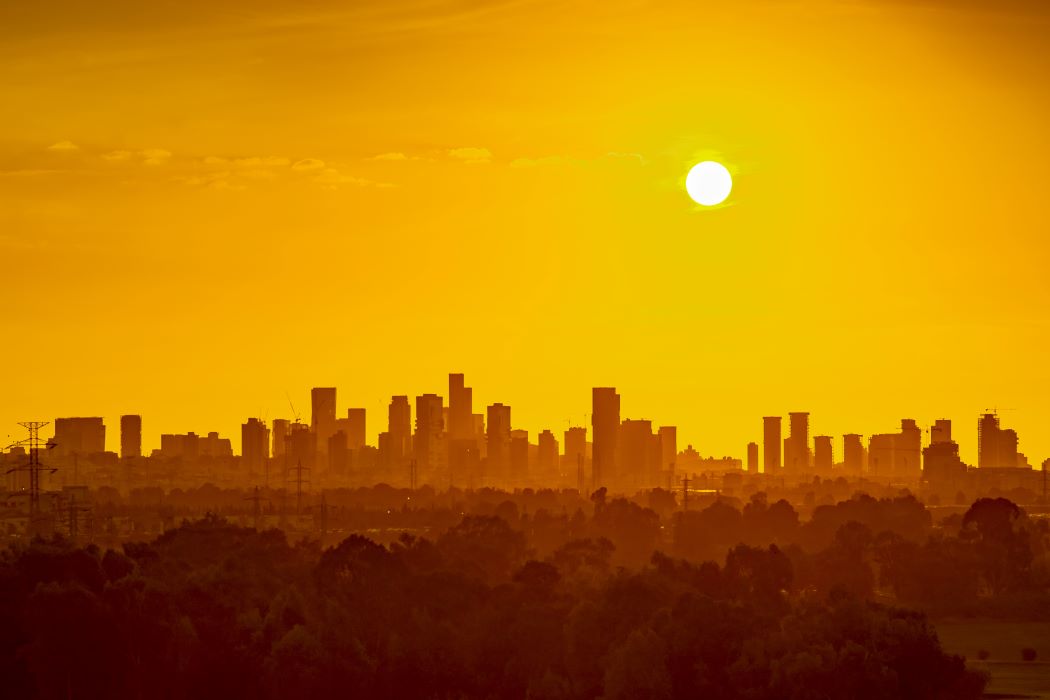 A city skyline in the distance with the sun shining in an orange hazy sky