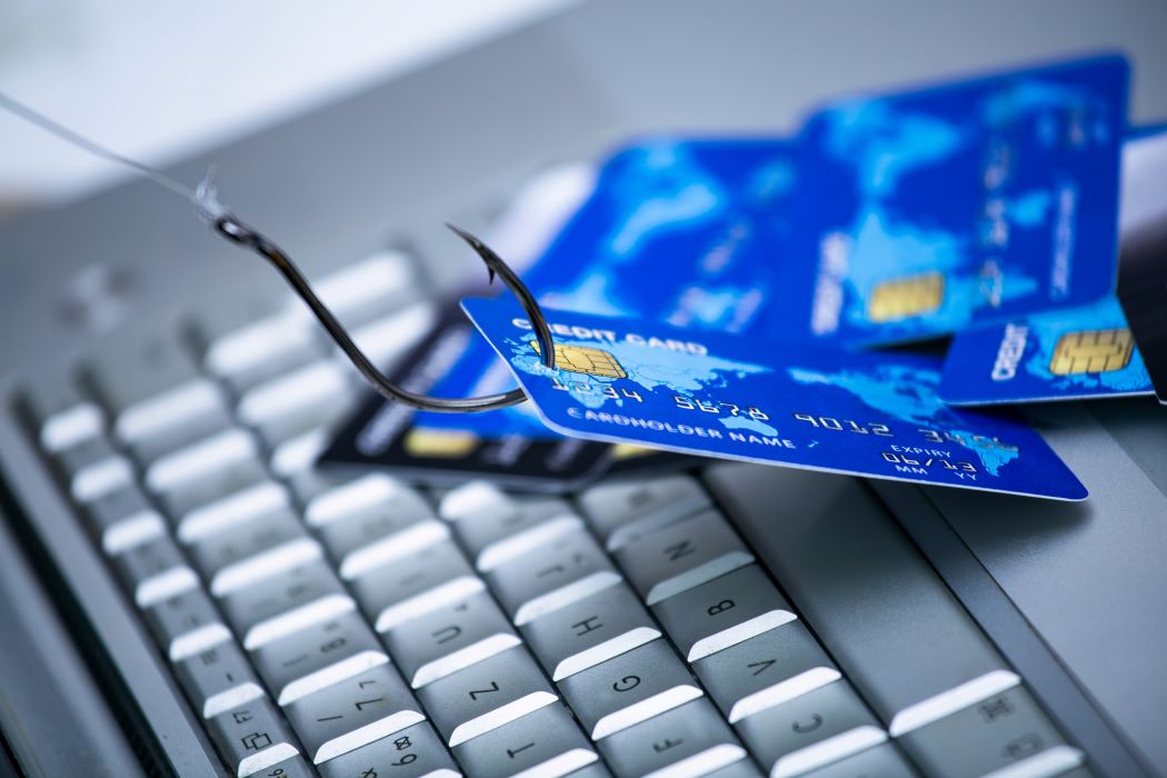 A fishing hook hooked onto a credit card above a laptop keyboard