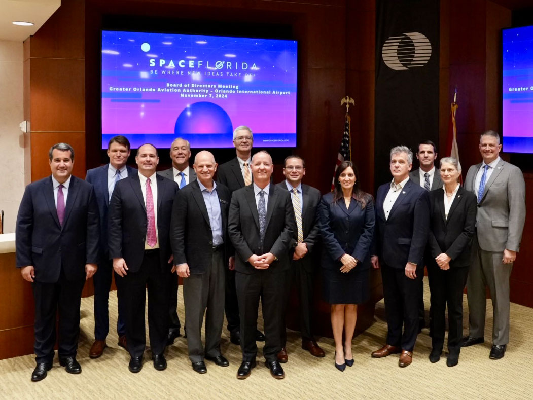 A group of people in suits standing in front of a screen that reads Space Florida.