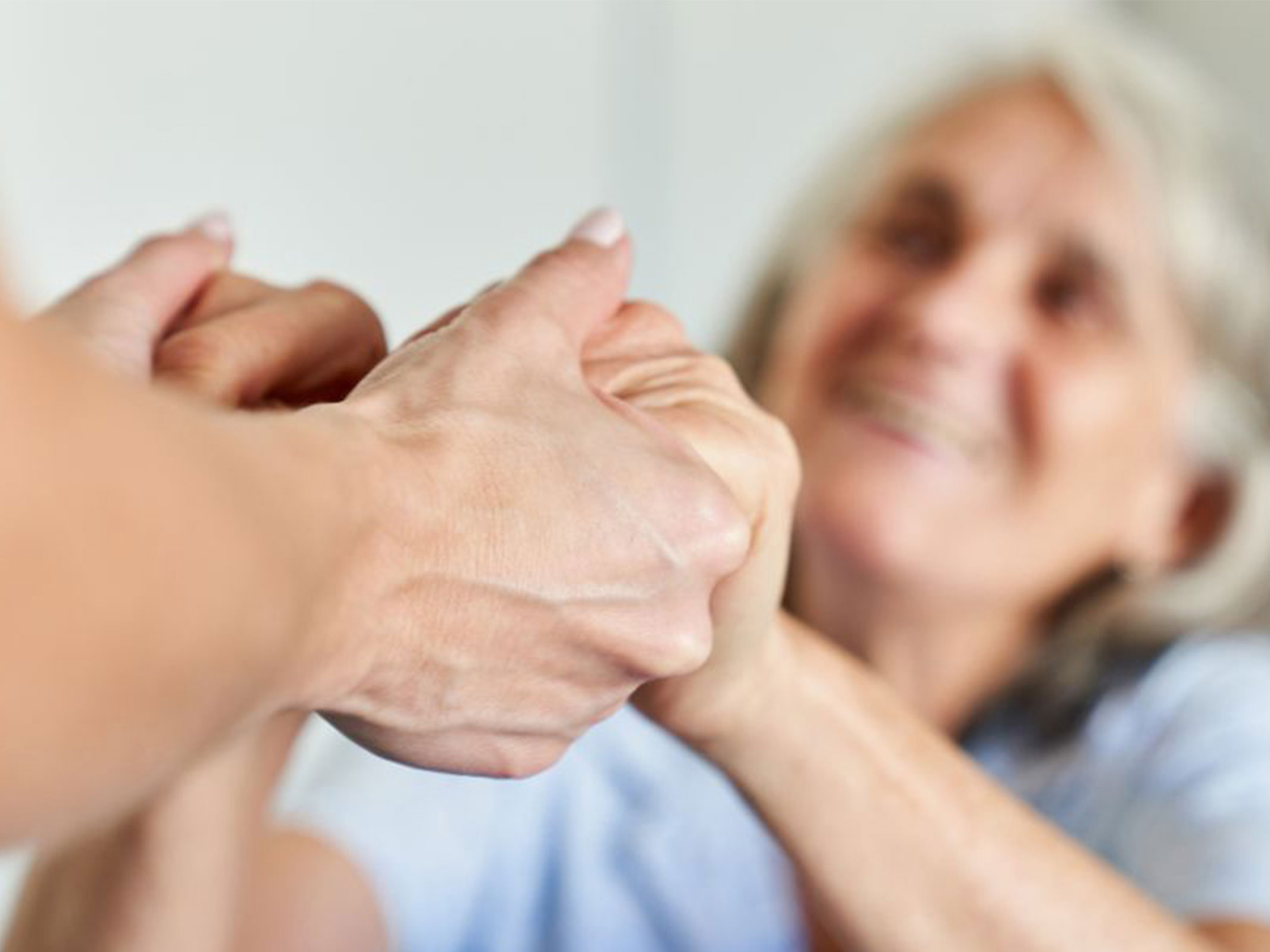 An older woman holds both hands of another individual out of frame.