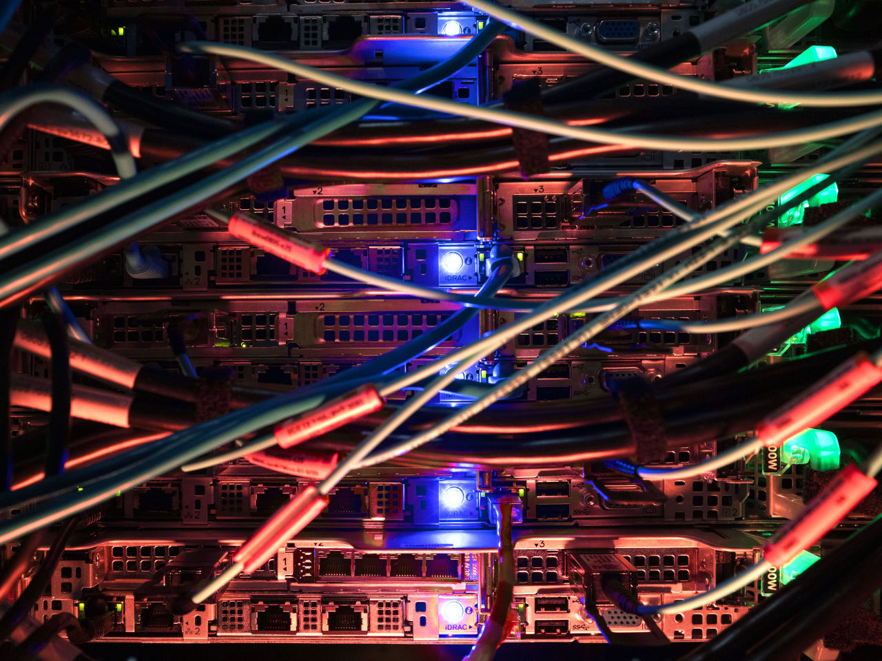 Wires criss-crossing the back of a server with blue and red lights illuminating the scene