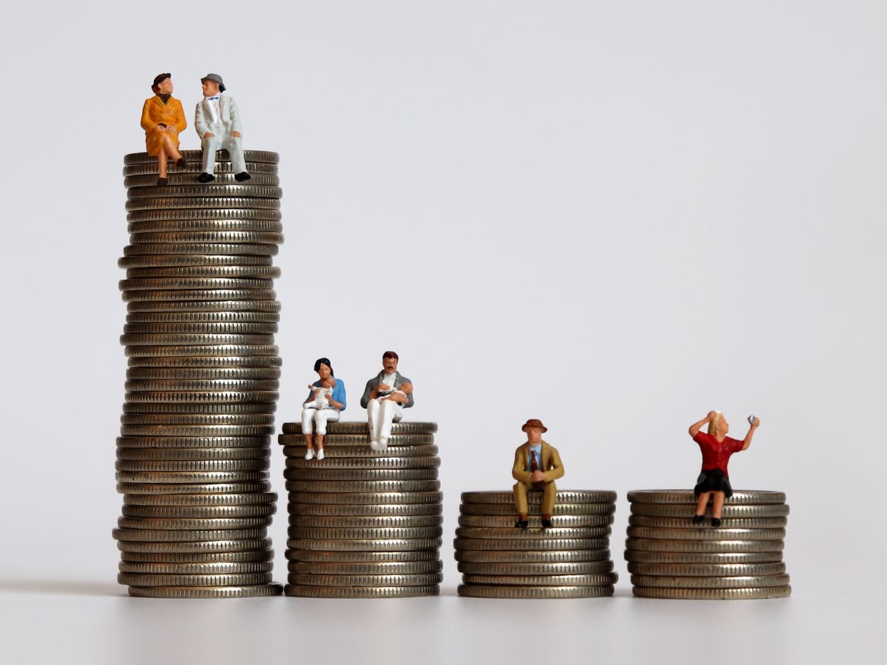 Small figurines of people sitting on unequal stacks of coins