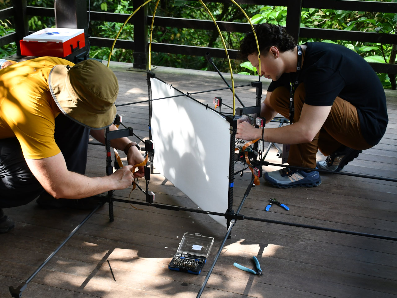 Researchers kneel onthe ground to adjust a research device made up of a white screen and other components