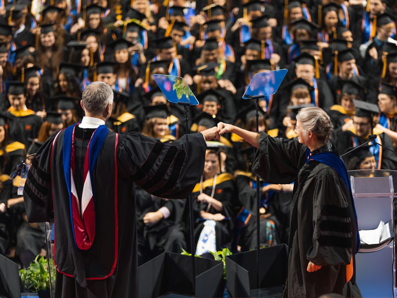 Rob Ferl and Anna-Lisa Paul give each other a fist bump while delivering a graduation speech.