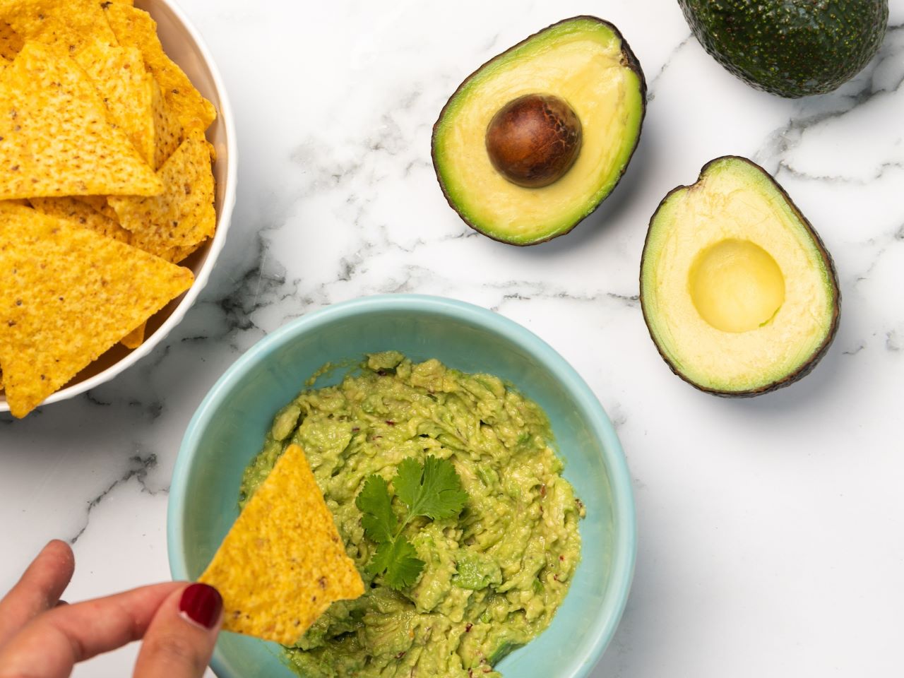 A top-down view of a hand dipping a tortilla chip into a bowl of guacamole