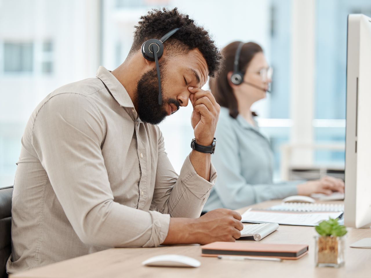 A call-center worker wearing a headset holds his head in frustration