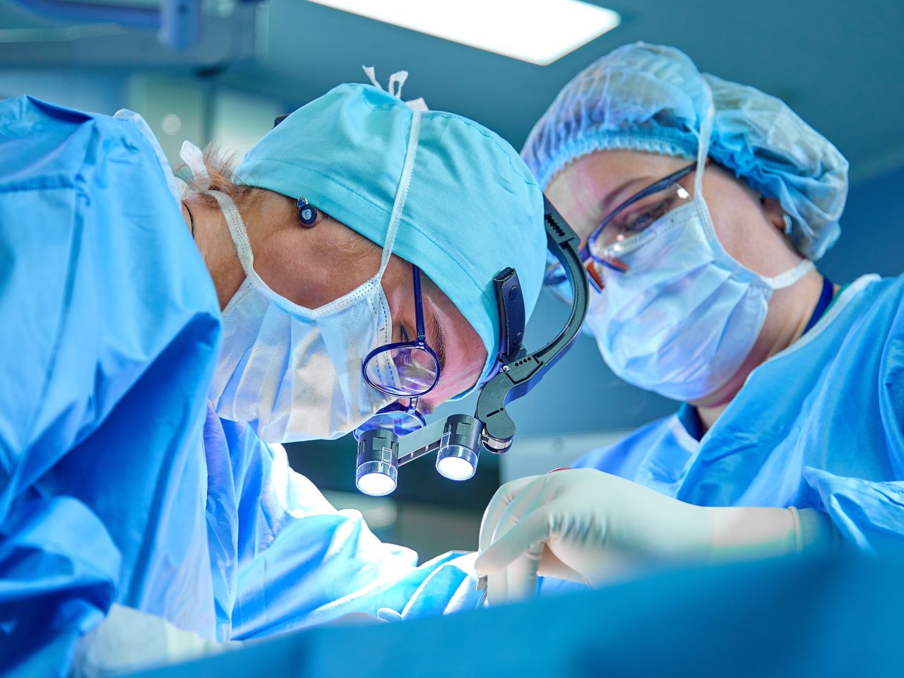 Two surgeons wearing scrubs look closely at an obscured patient during a procedure