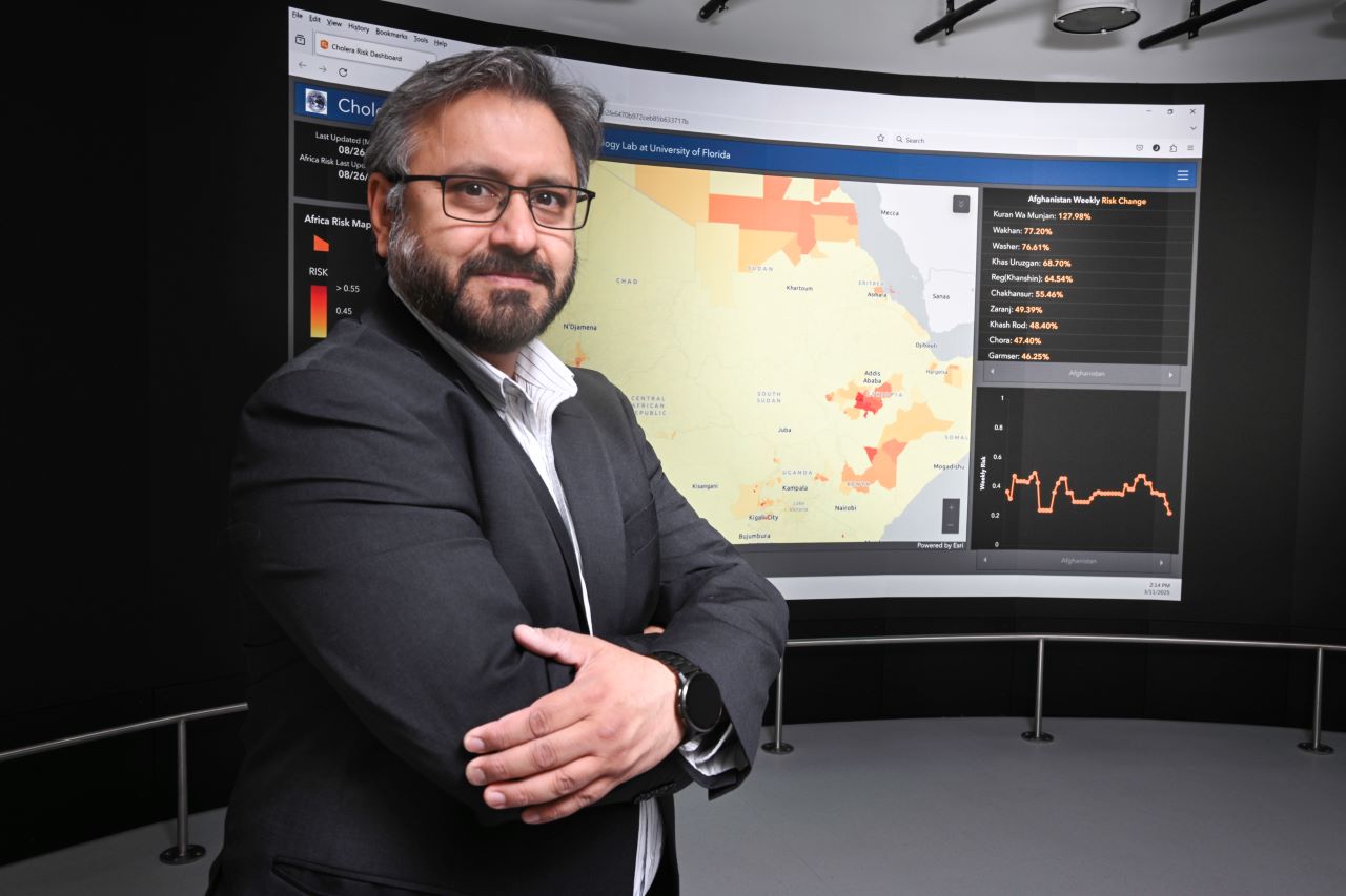 Professor Jutla stands in front of large computer screen displaying Cholera Risk Dashboard