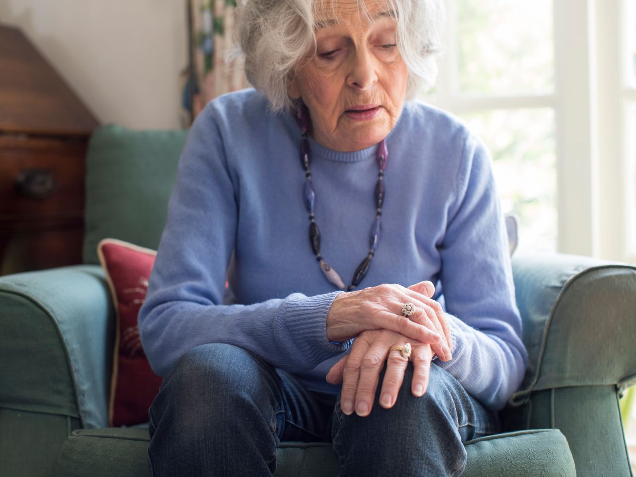 An older woman sitting on a chair and grasping one hand with another