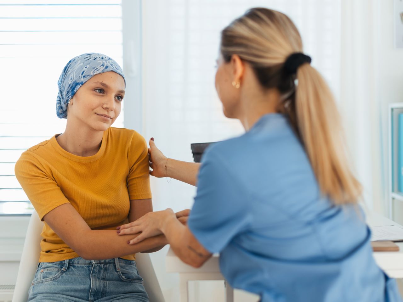 A teenaged cancer patient wearing a bandana on her head is touched warmly by a doctor