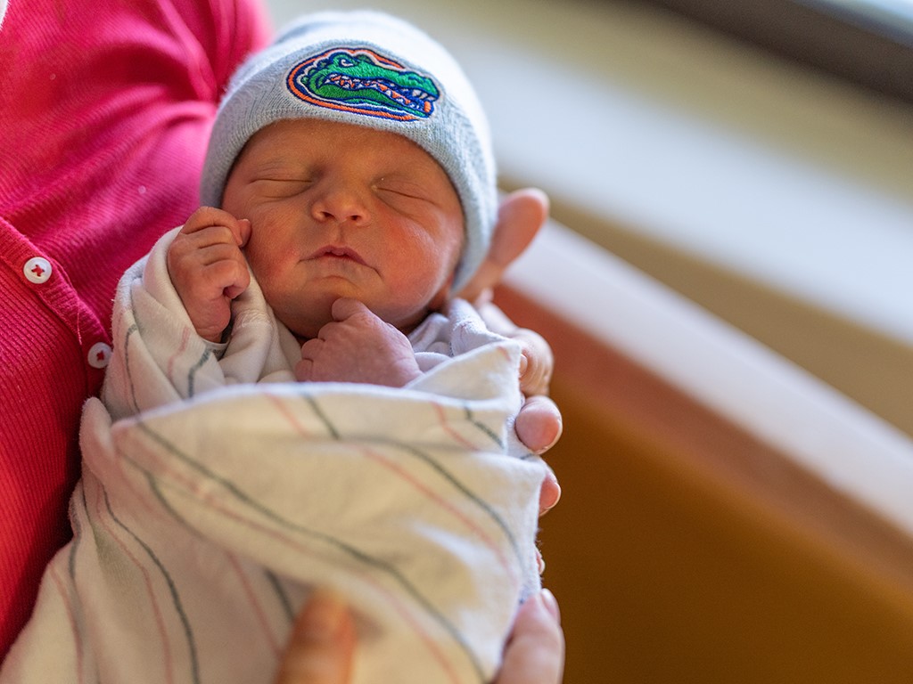 A swaddled newborn baby wearing a Florida Gators beanie