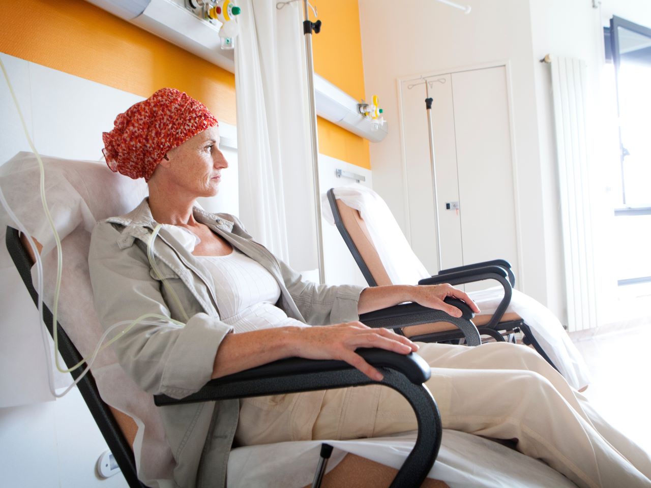 A woman wearing a read head scarf sits in a chemotherapy treatment chair in a hospital