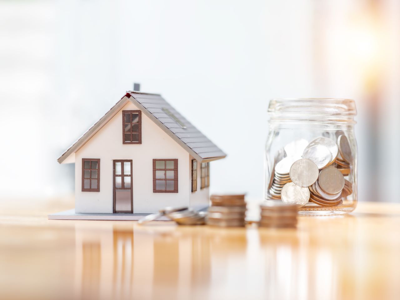 A small paper model house next to a jar filled with quarters