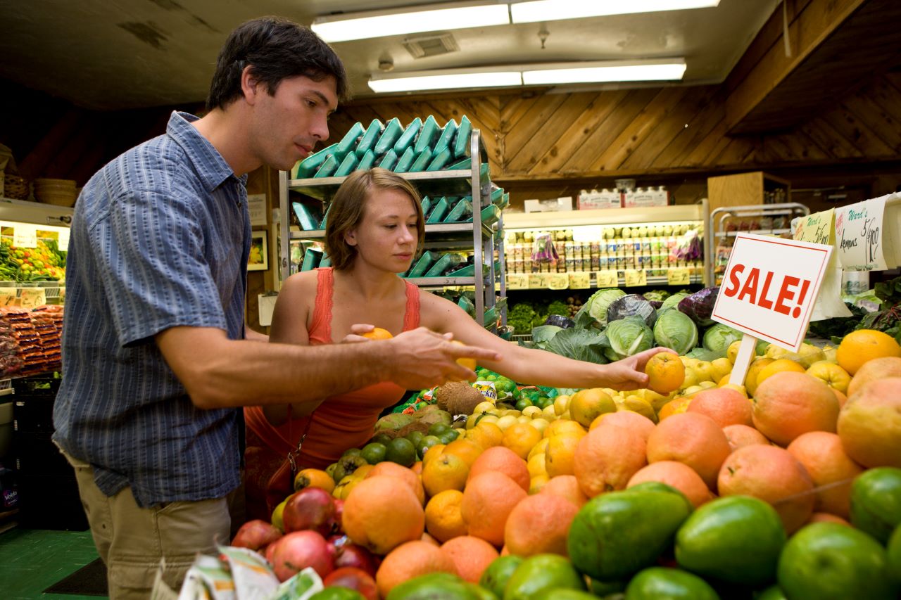 a man and a woman pick out citrus in the produce section of grocery store